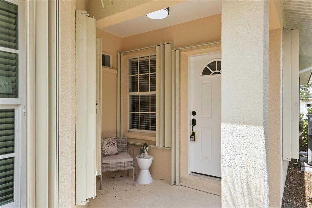 A covered front porch features a white door, a window with accordion shutters, and seating — 503 AUBURN COVE CIRCLE, VENICE, FL