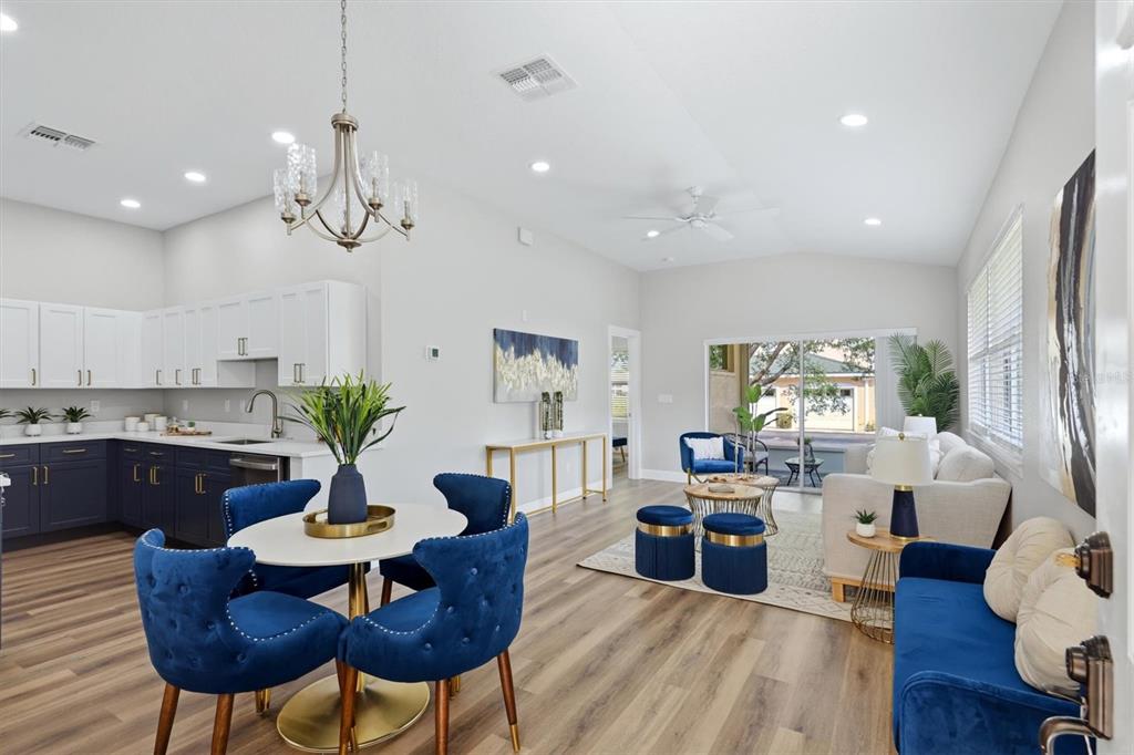An open-concept kitchen, dining area, and living room feature blue velvet furniture and wood flooring — 503 AUBURN COVE CIRCLE, VENICE, FL
