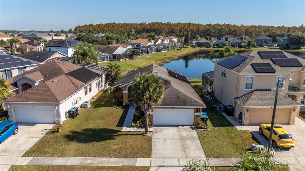 An aerial view shows three suburban houses with solar panels and garages near a pond — 1611 BRIDGEVIEW CIRCLE, ORLANDO, FL