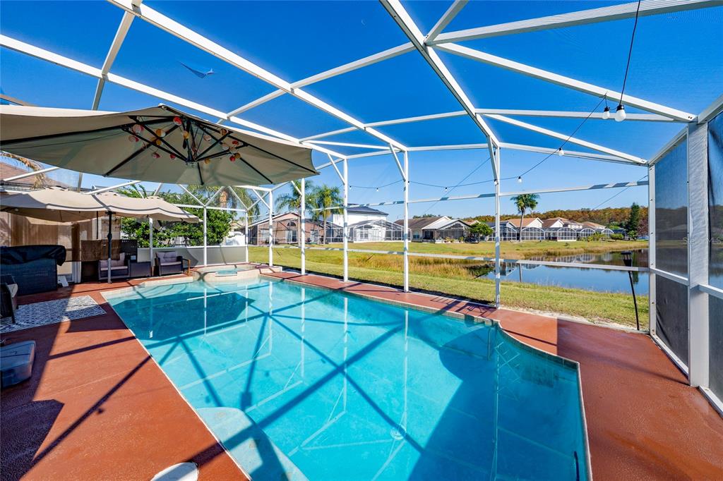 A screened-in swimming pool with a patio area overlooks a pond and neighboring houses — 1611 BRIDGEVIEW CIRCLE, ORLANDO, FL