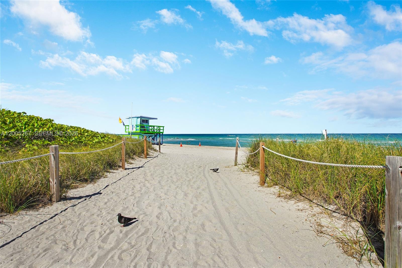 A sandy path leads through dunes toward a lifeguard tower on a sunny beach — 6917 Collins Ave # 820, Miami Beach FL 33141, MIAMI BEACH, FL