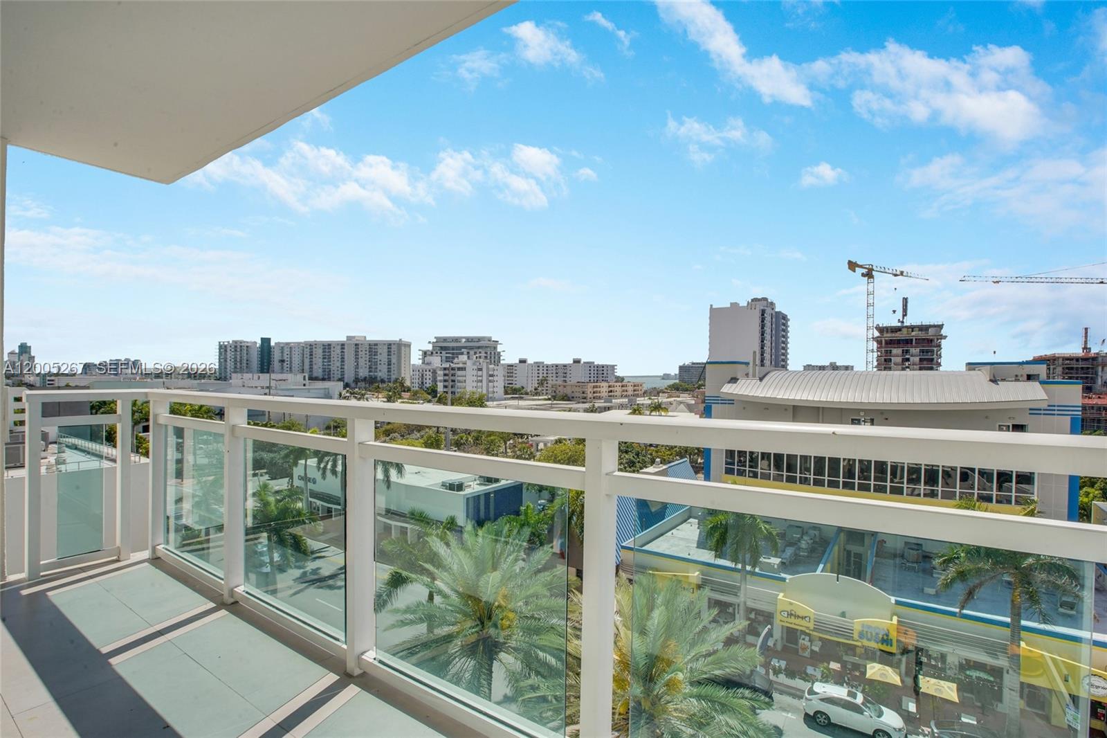 A balcony with a glass railing overlooks a city street with palm trees and buildings — 6917 Collins Ave # 820, Miami Beach FL 33141, MIAMI BEACH, FL