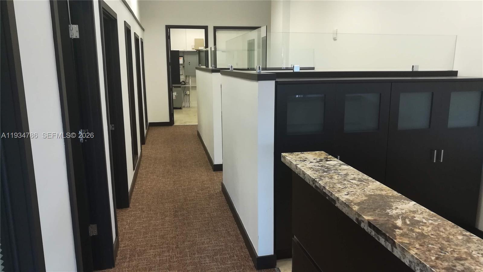 An office hallway features dark cabinetry, a granite countertop, and glass-topped partition walls — 2030 S Douglas Rd # 109, Coral Gables FL 33134, CORAL GABLES, FL