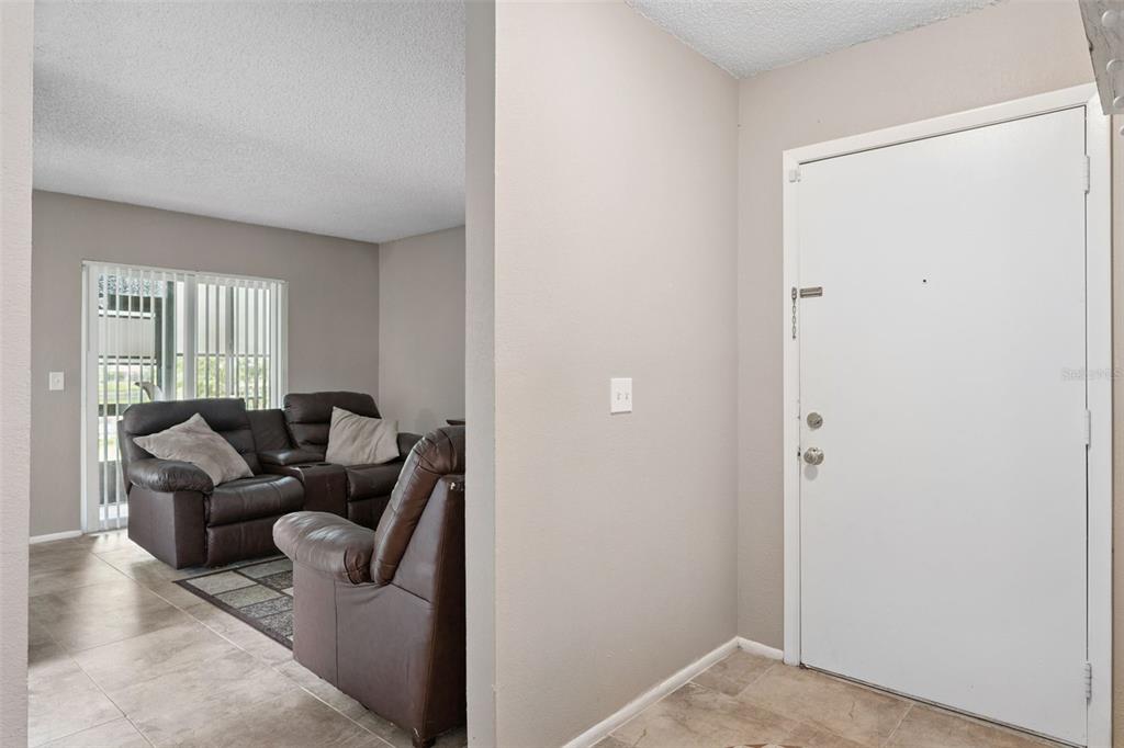 An entryway with tile flooring leads into a living room featuring a brown leather sofa — 2417 BARLEY CLUB COURT UNIT 1, ORLANDO, FL