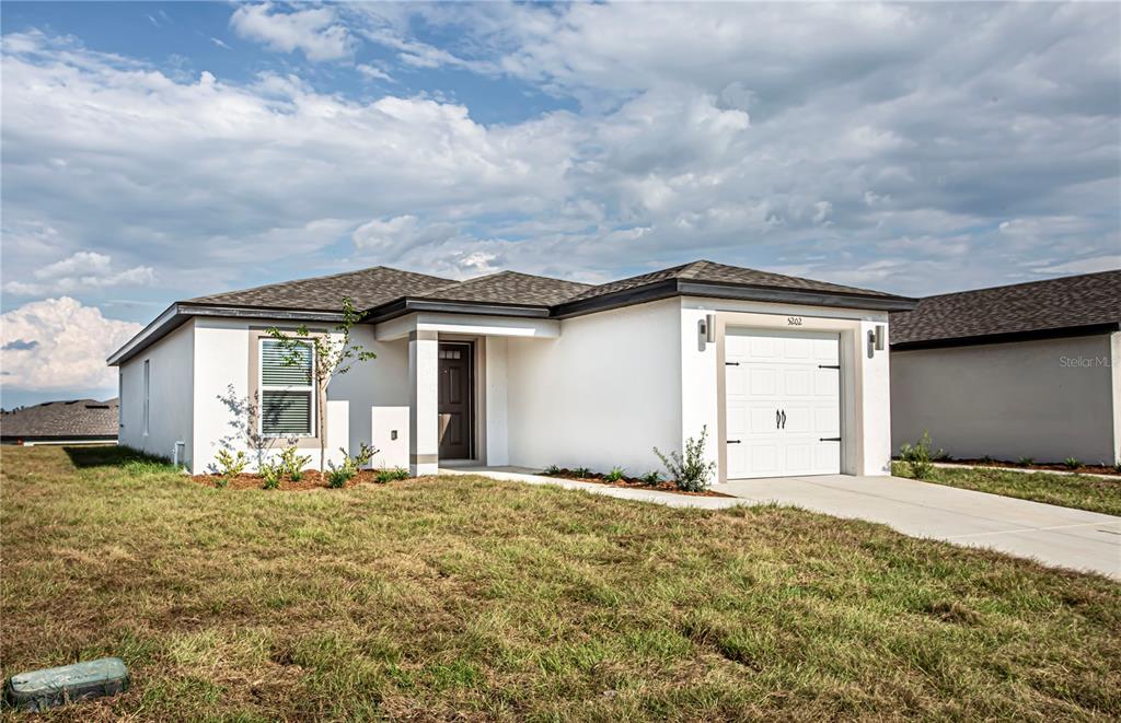 A single-story white house with a garage and a small front yard under a cloudy sky — 5202 SAILOR ROAD, BROOKSVILLE, FL