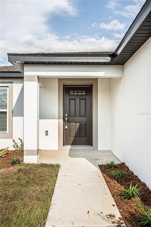 A concrete walkway leads to the front entrance of a house with a dark door — 5202 SAILOR ROAD, BROOKSVILLE, FL