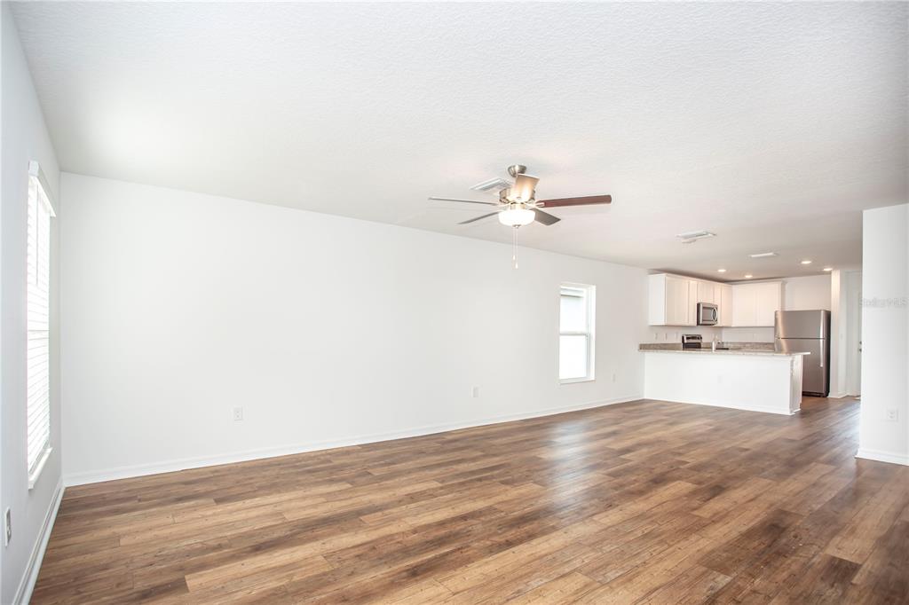 An open-concept living area with white walls, wood-look flooring, and an adjacent kitchen — 5202 SAILOR ROAD, BROOKSVILLE, FL