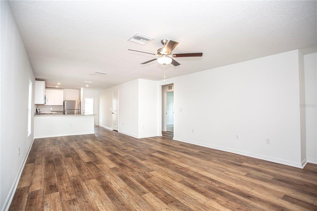 An open-concept living area features wood-look flooring, white walls, and a kitchen in the background — 5202 SAILOR ROAD, BROOKSVILLE, FL