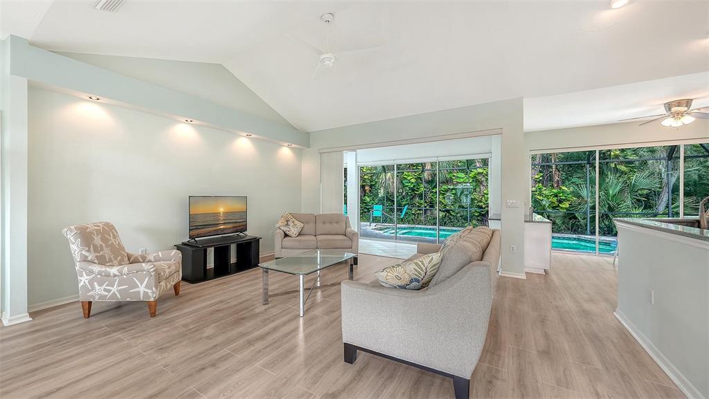 A living room with light wood floors, vaulted ceilings, and sliding doors opening to a pool — 2929 SANDRINGHAM PLACE, SARASOTA, FL