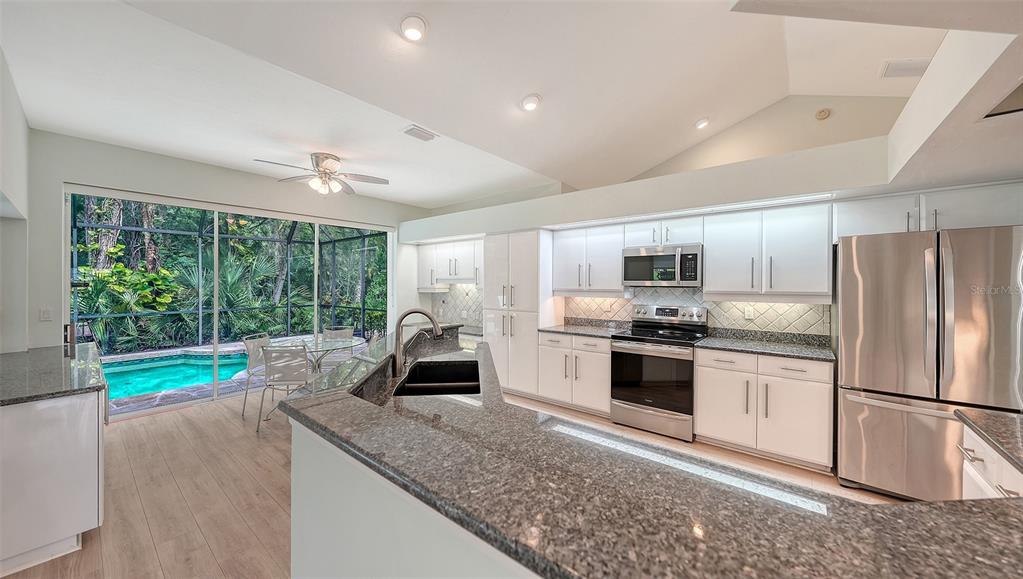 A kitchen with white cabinets, granite countertops, and a view of a screened-in swimming pool — 2929 SANDRINGHAM PLACE, SARASOTA, FL