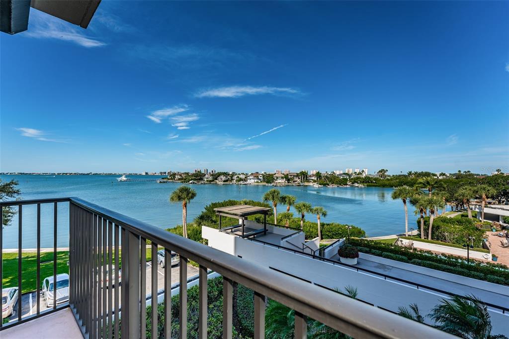 A balcony overlooks a bay with palm trees, a parking lot, and distant buildings — 6 BELLEVIEW BOULEVARD UNIT 306, BELLEAIR, FL