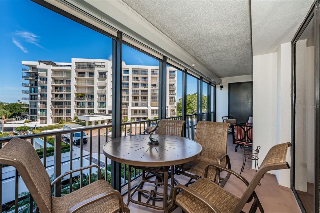 A screened-in balcony features a round metal table with four chairs overlooking a large building — 6 BELLEVIEW BOULEVARD UNIT 306, BELLEAIR, FL