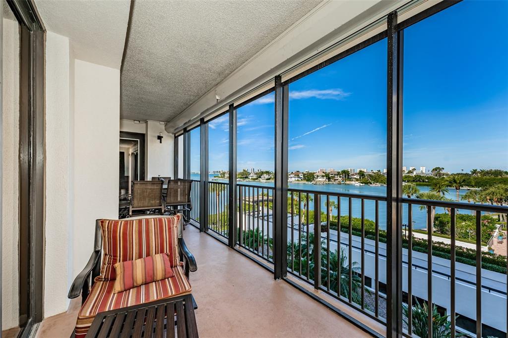 A screened-in balcony features a striped chair and a view of the water and coastline — 6 BELLEVIEW BOULEVARD UNIT 306, BELLEAIR, FL