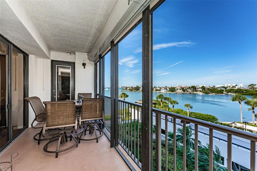 A screened balcony features patio furniture overlooking a bay with palm trees and distant buildings — 6 BELLEVIEW BOULEVARD UNIT 306, BELLEAIR, FL