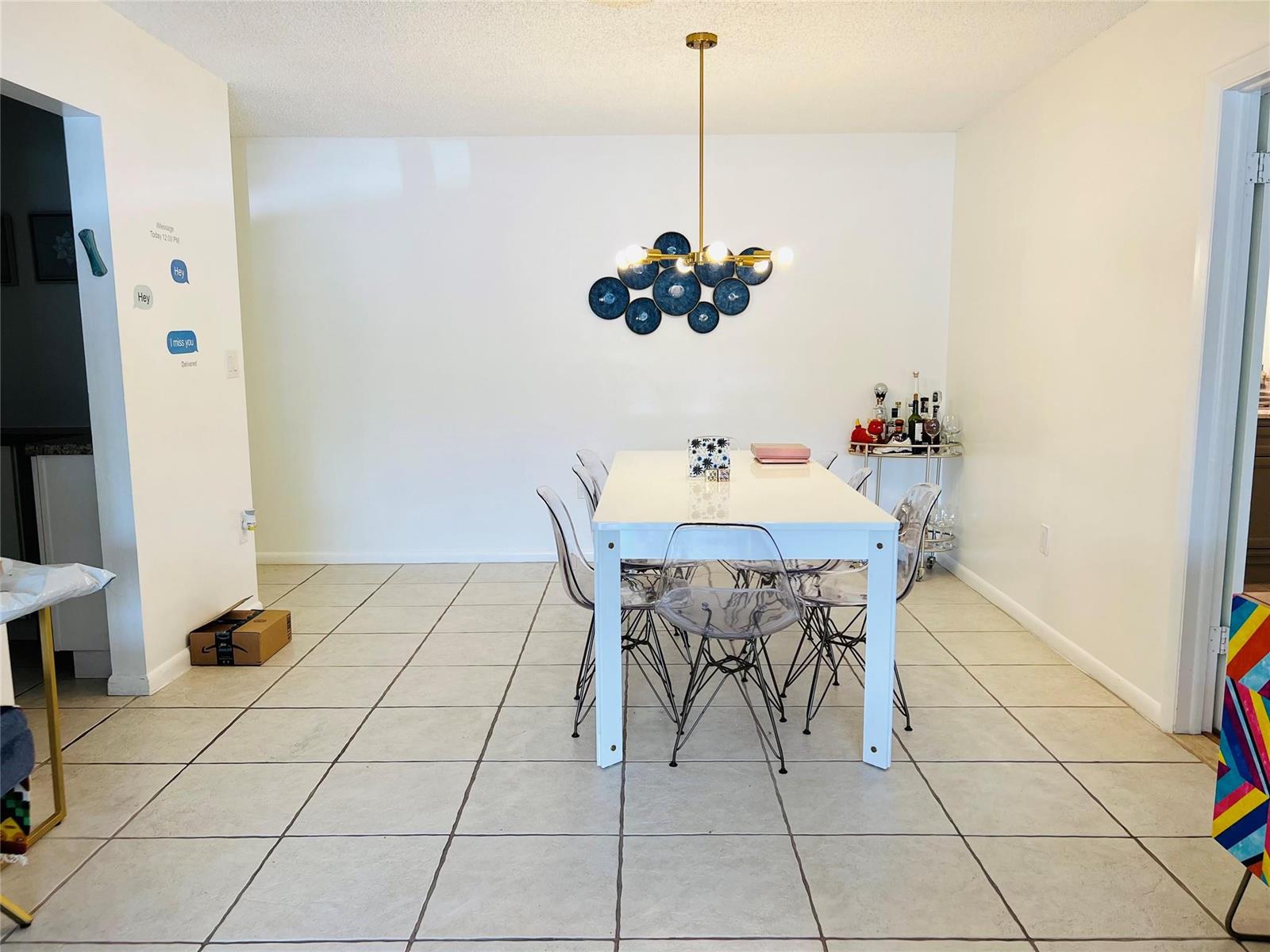 A dining room features a white table, clear chairs, a gold chandelier, and tile flooring — 4040 N Hills Drive # 7, Hollywood FL 33021, HOLLYWOOD, FL
