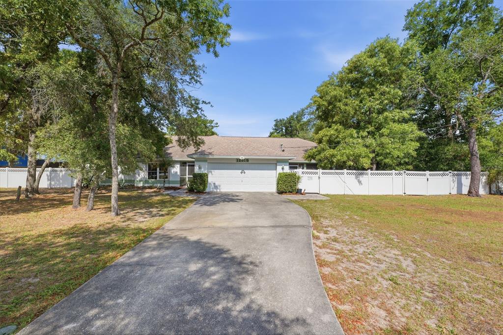 A single-story house with a white garage and a concrete driveway surrounded by trees — 12515 CANTON AVENUE, HUDSON, FL