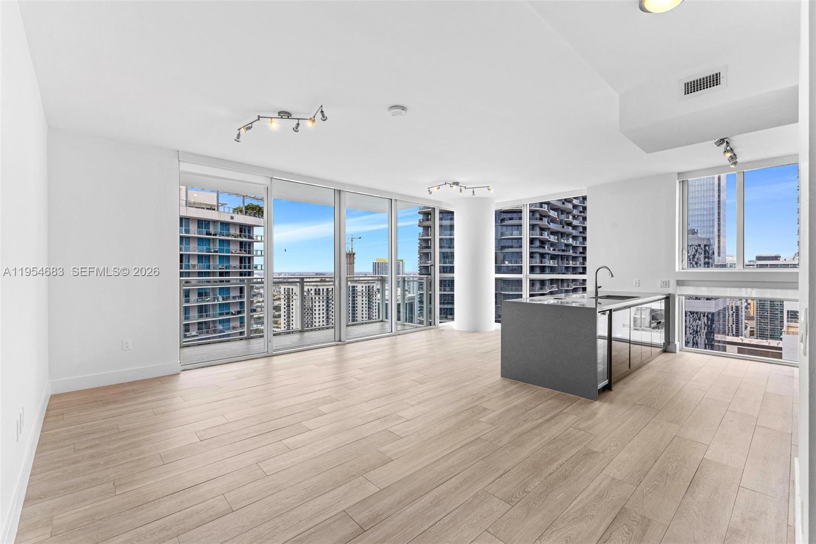 A modern, open-concept living area features light wood floors, a kitchen island, and floor-to-ceiling windows — 1080 Brickell Ave # 3909, Miami FL 33131, MIAMI, FL