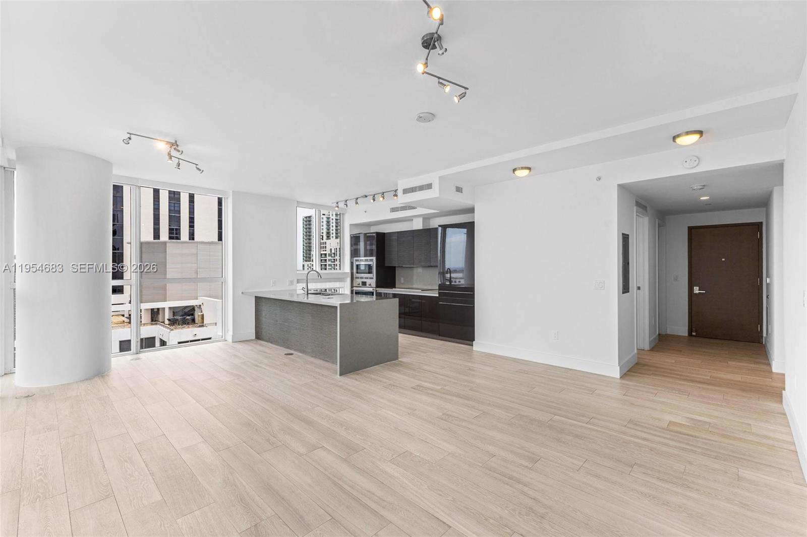 This open-concept living area features light wood flooring, a modern kitchen island, and floor-to-ceiling windows — 1080 Brickell Ave # 3909, Miami FL 33131, MIAMI, FL