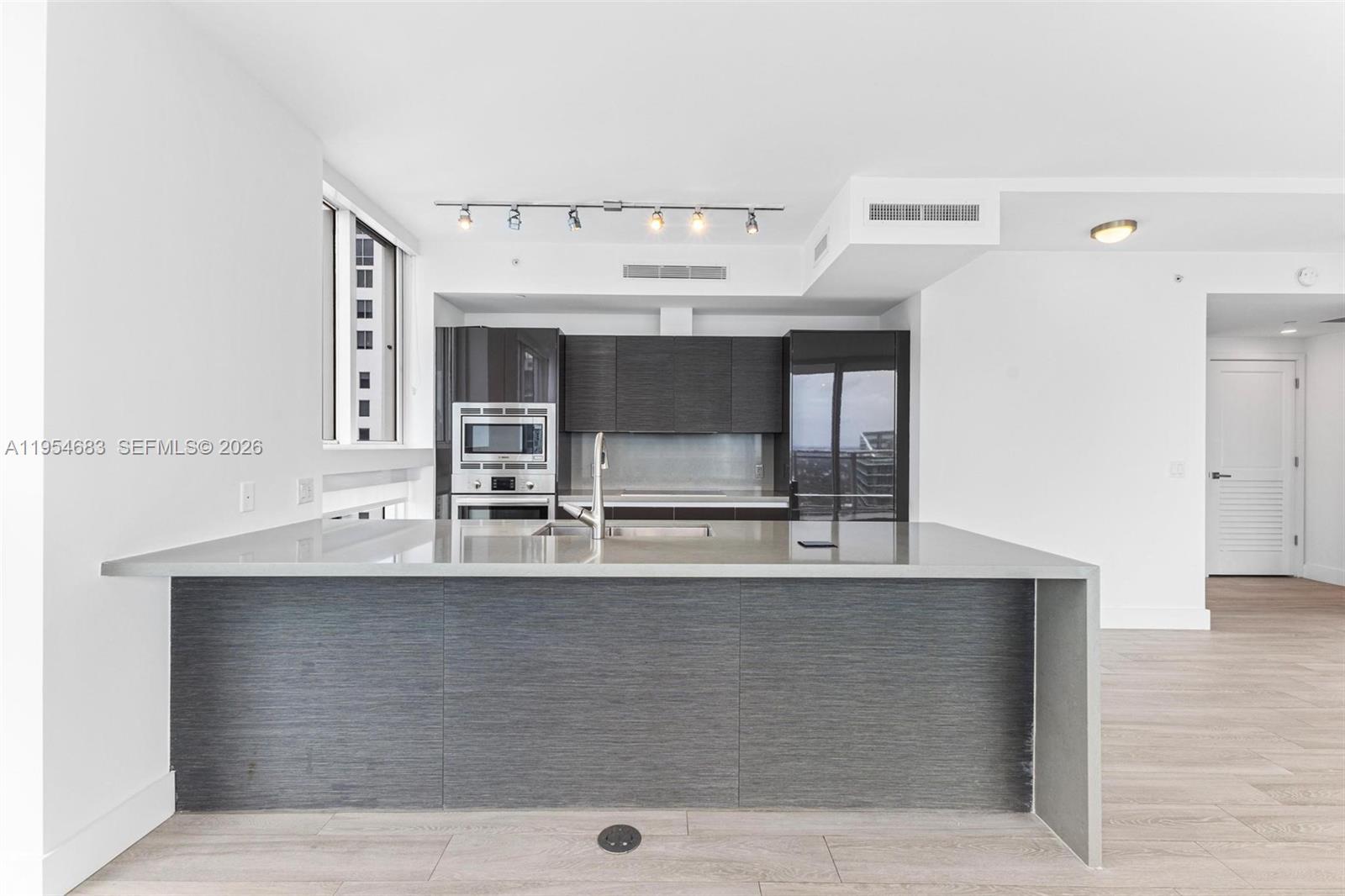 A modern kitchen features a large gray island, dark cabinetry, and light wood-look flooring — 1080 Brickell Ave # 3909, Miami FL 33131, MIAMI, FL