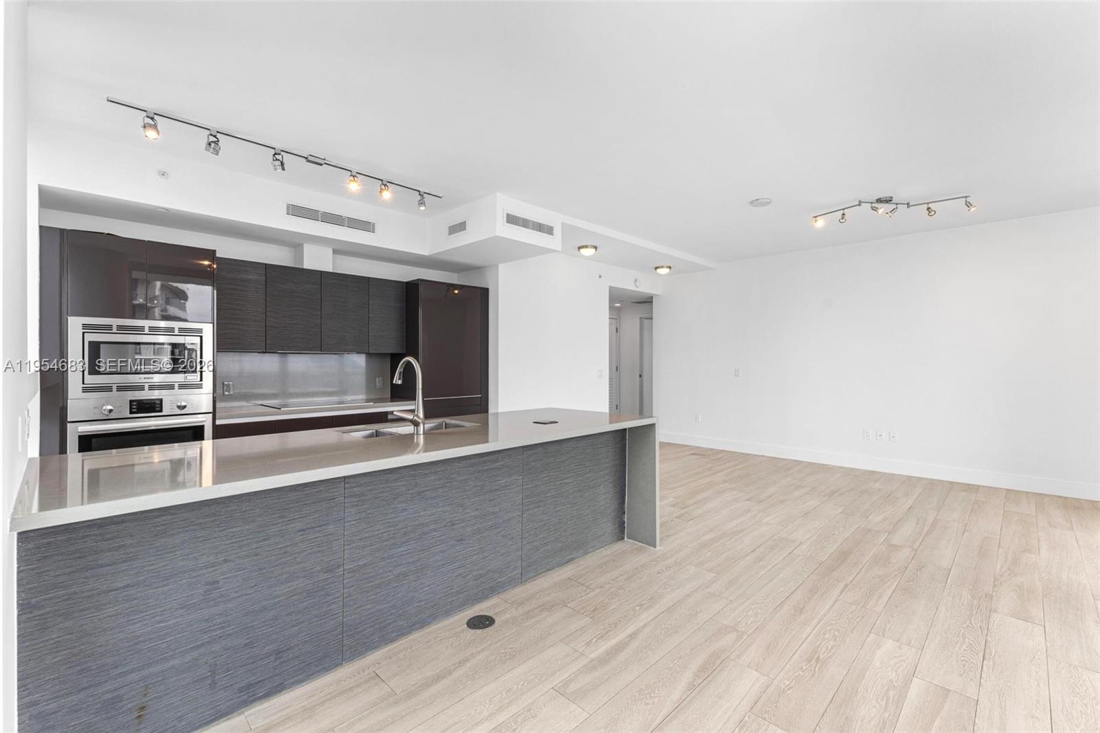 A modern kitchen with dark cabinetry and a large island opens into a living area — 1080 Brickell Ave # 3909, Miami FL 33131, MIAMI, FL