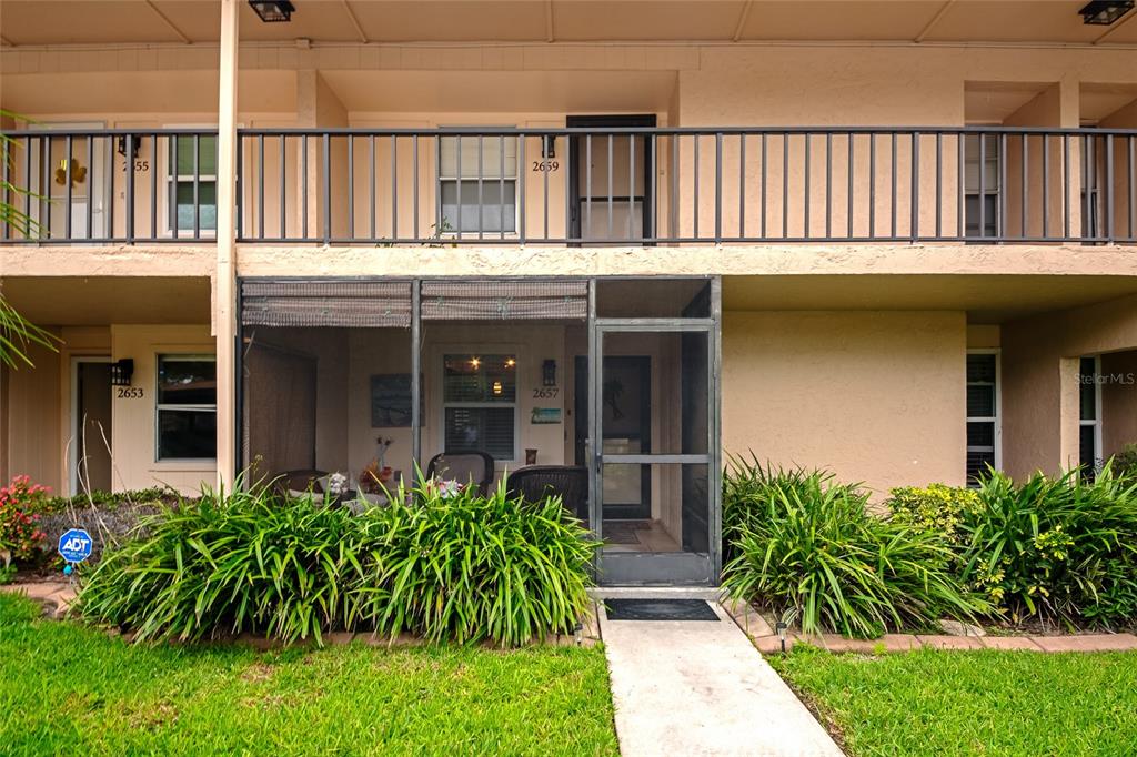 A two-story apartment building exterior features a ground-level screened patio and a second-floor balcony — 2657 WOODGATE LANE UNIT E4, SARASOTA, FL