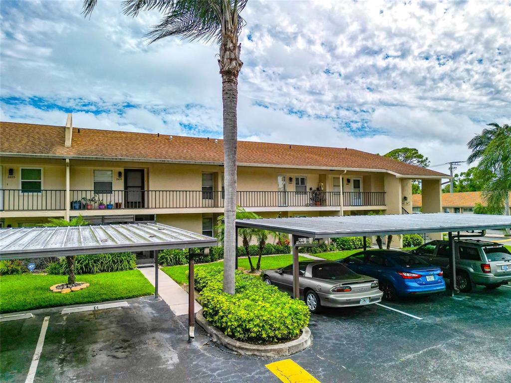 A two-story apartment building with covered parking spaces and a palm tree in front — 2657 WOODGATE LANE UNIT E4, SARASOTA, FL