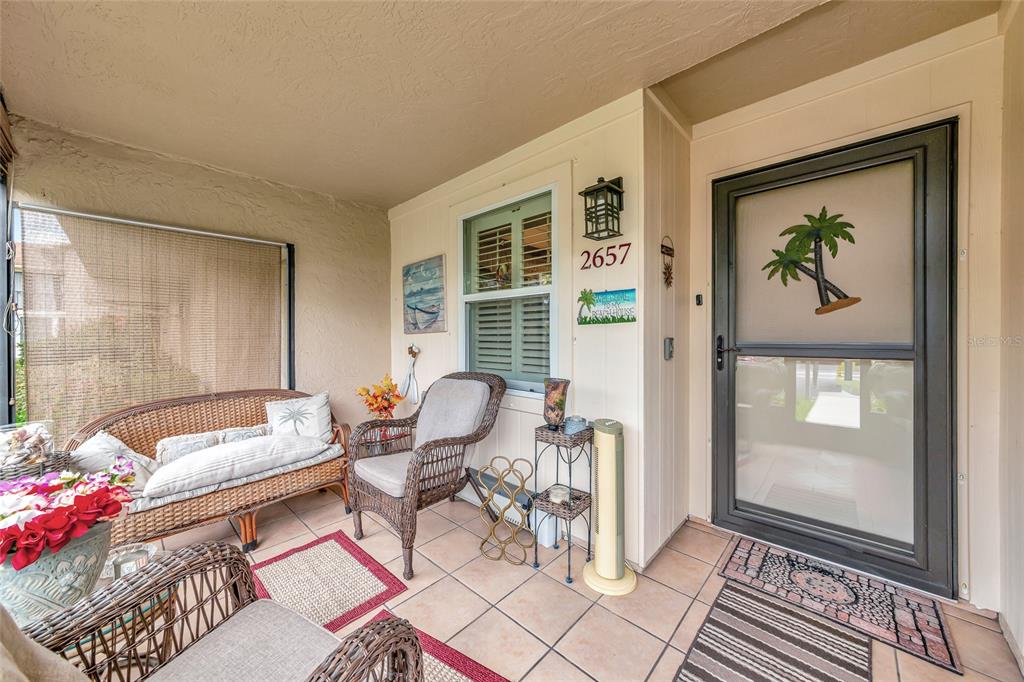 A covered patio features wicker furniture, tiled flooring, and a glass storm door — 2657 WOODGATE LANE UNIT E4, SARASOTA, FL