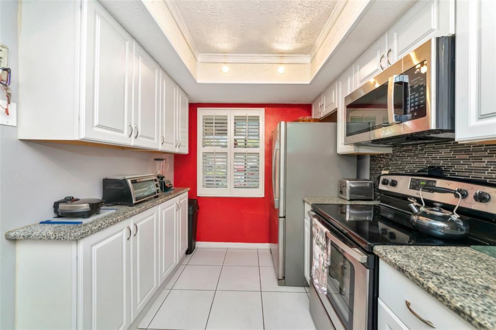 A galley kitchen features white cabinets, granite countertops, stainless steel appliances, and a red wall — 2657 WOODGATE LANE UNIT E4, SARASOTA, FL