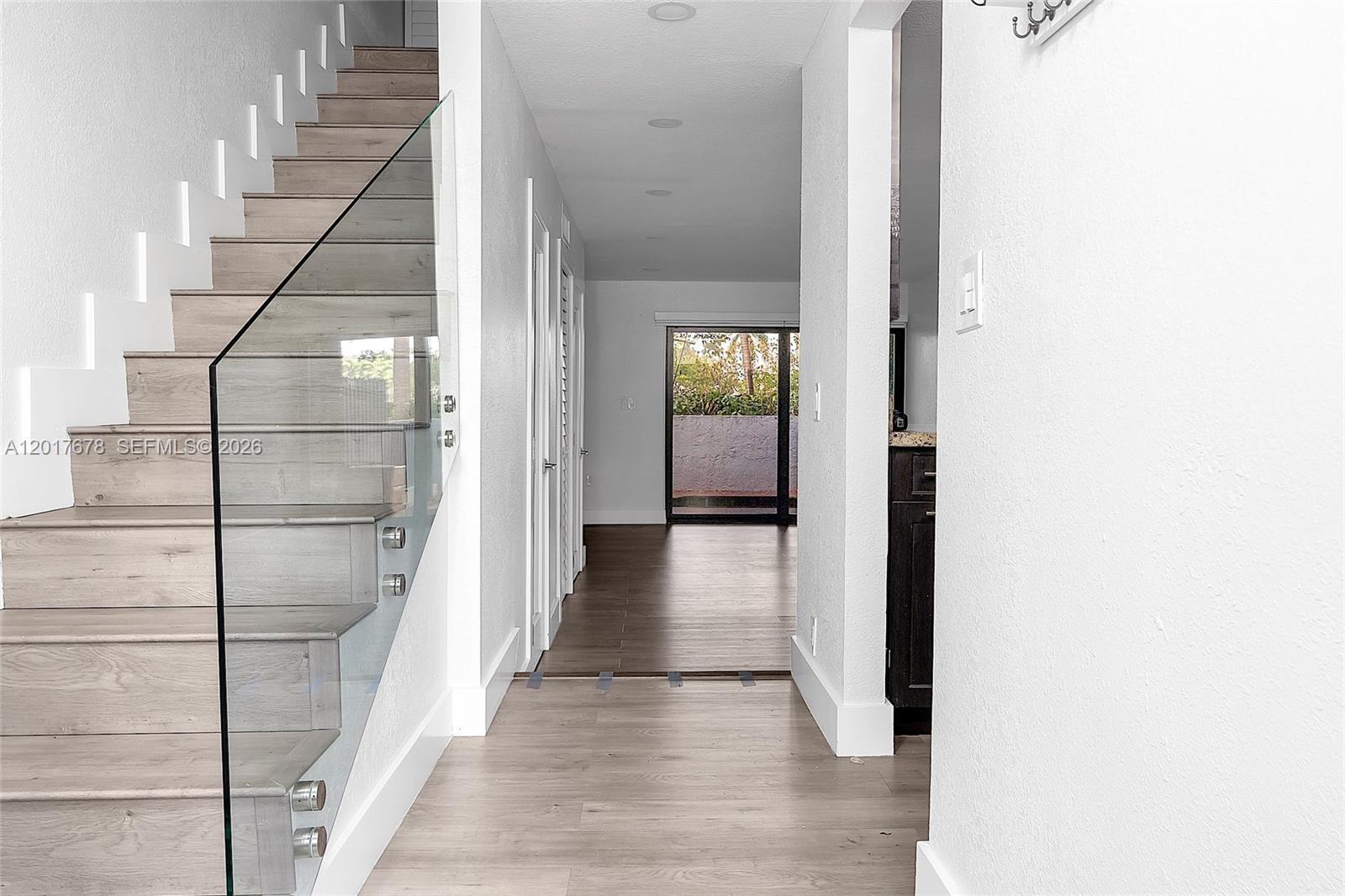 A hallway features light wood flooring, a glass-railed staircase, and a view toward a patio — 1901 NW S River Dr # 28C, Miami FL 33125, MIAMI, FL