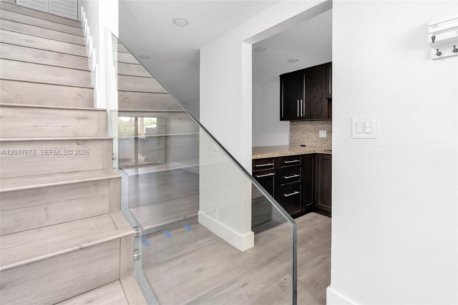 A staircase with light wood steps and a glass railing leads toward a dark-cabinet kitchen — 1901 NW S River Dr # 28C, Miami FL 33125, MIAMI, FL