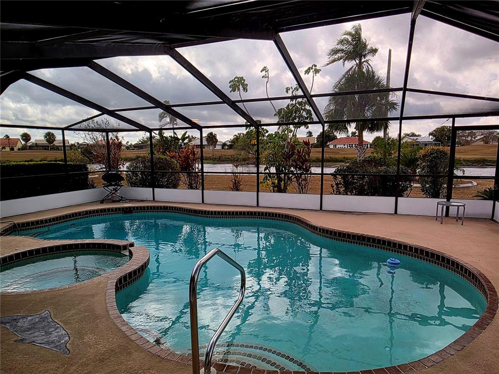 A screened-in pool and hot tub overlook a grassy yard and a body of water — 1924 NEW BEDFORD DRIVE, SUN CITY CENTER, FL