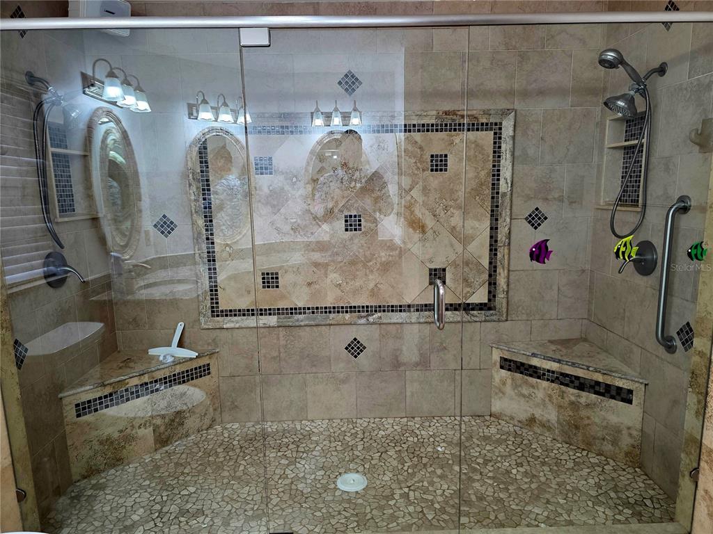 A walk-in shower features stone tile walls, a pebble floor, dual benches, and glass doors — 1924 NEW BEDFORD DRIVE, SUN CITY CENTER, FL