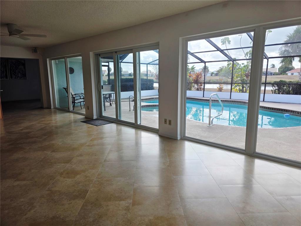 A living room with large tile floors features sliding glass doors overlooking a pool area — 1924 NEW BEDFORD DRIVE, SUN CITY CENTER, FL