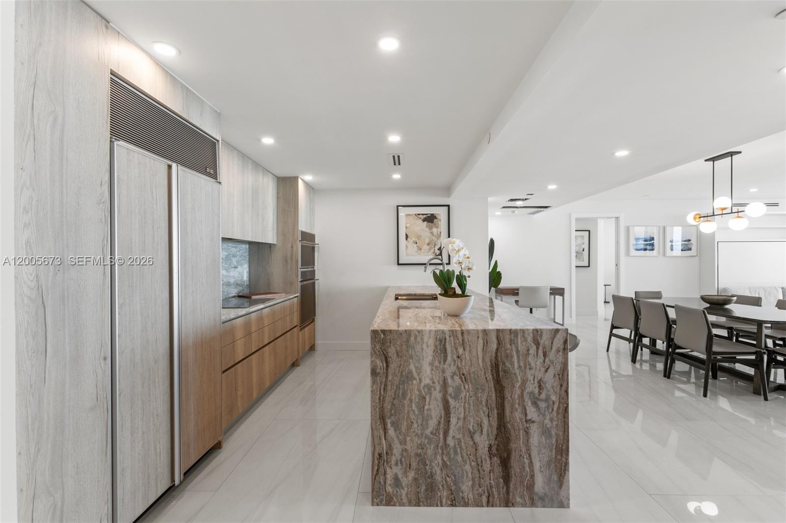 A modern kitchen features a large stone waterfall island, wood cabinetry, and white tile flooring — 1500 Ocean Dr # 1003, Miami Beach FL 33139, MIAMI BEACH, FL