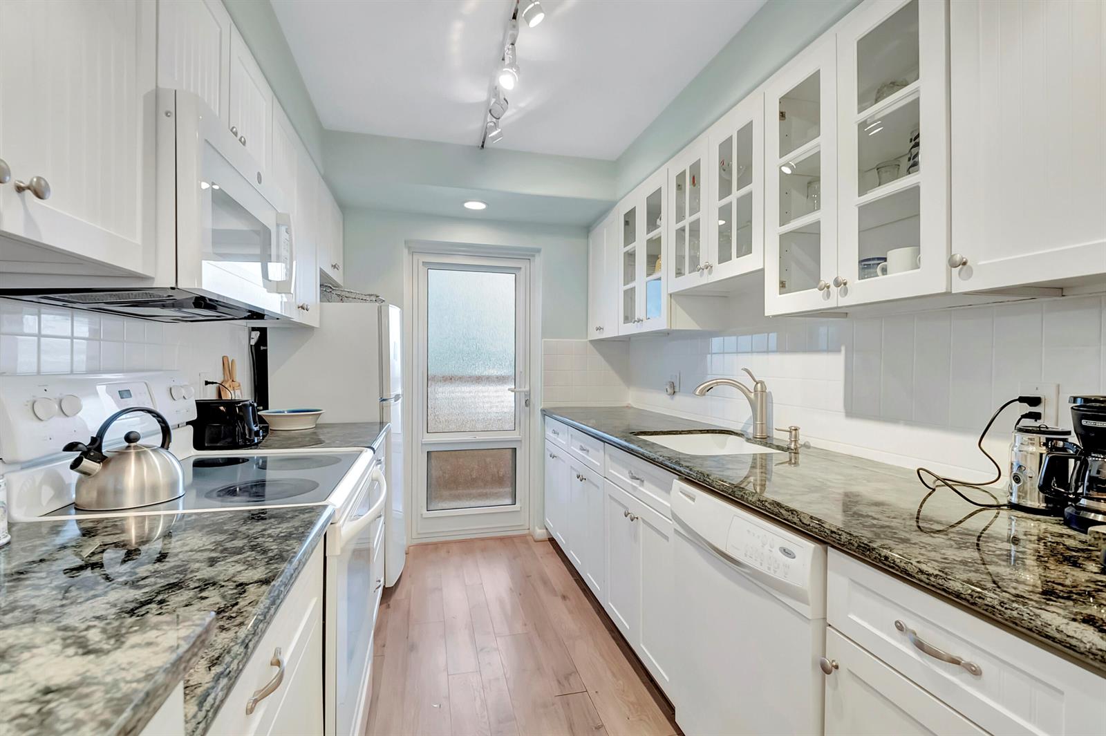 A galley kitchen features white cabinets, dark granite countertops, stainless steel appliances, and wood flooring — 1910 S Ocean Boulevard # 416, Delray Beach FL 33483, DELRAY BEACH, FL