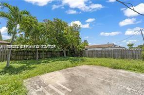 A backyard features a concrete patio, a wooden fence, and several trees under a sky — 303 NW 7th St # 2, Hallandale Beach FL 33009, HALLANDALE BEACH, FL