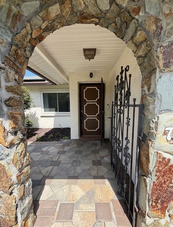 A stone archway frames a paved entryway leading to a brown door with decorative trim — 7438 LAKE FOREST CIRCLE, PORT RICHEY, FL