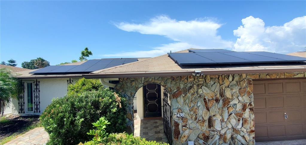 A single-story house exterior features a stone facade, a garage, and roof-mounted solar panels — 7438 LAKE FOREST CIRCLE, PORT RICHEY, FL