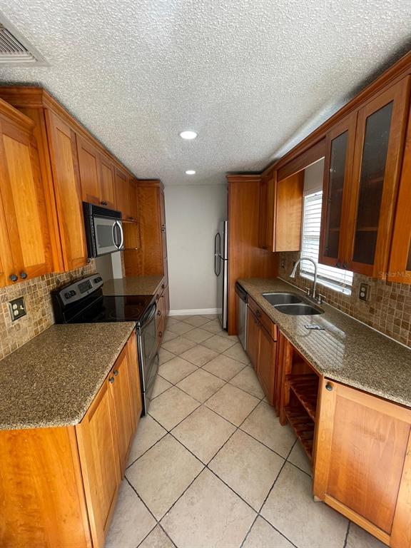 A galley kitchen features wood cabinets, granite countertops, tile backsplash, and tile flooring — 6218 YORKTOWN DRIVE UNIT 15, ORLANDO, FL