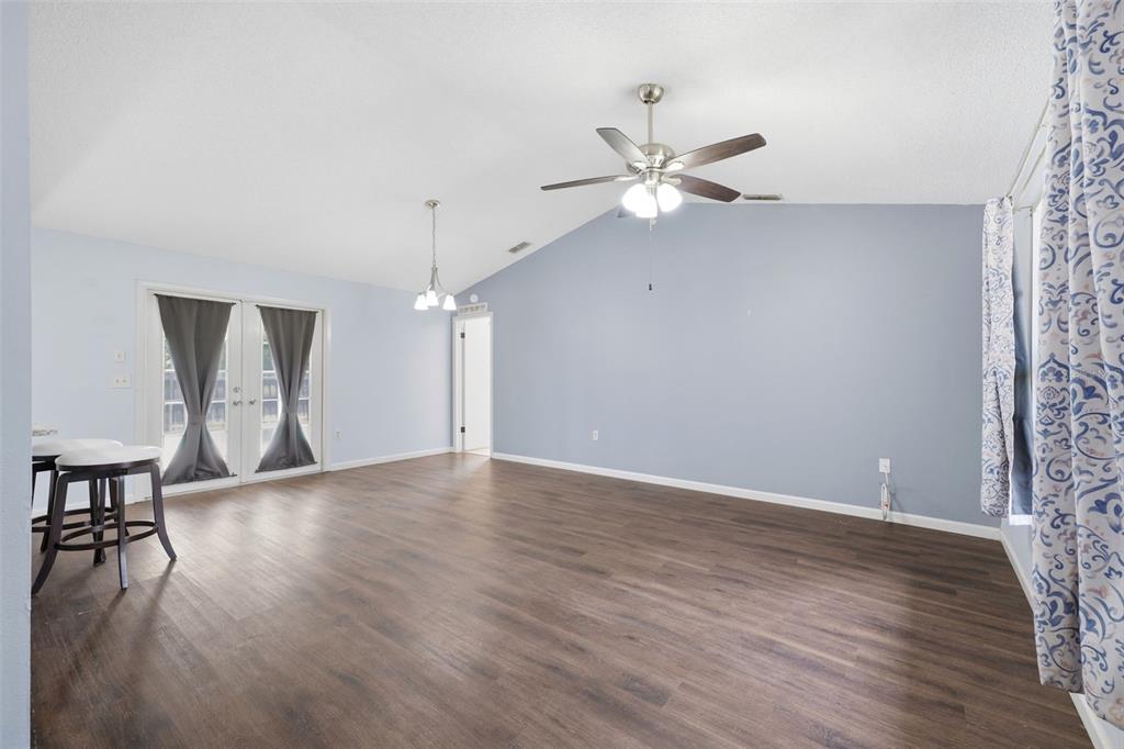 A spacious room with light blue walls, dark wood-look flooring, a vaulted ceiling, and ceiling fan — 8178 ENGLISH ELM CIRCLE, SPRING HILL, FL