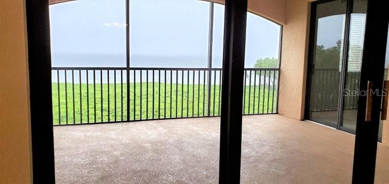 A covered balcony with a screen enclosure overlooks a grassy area and the ocean — 91 VIVANTE BOULEVARD UNIT 9133, PUNTA GORDA, FL