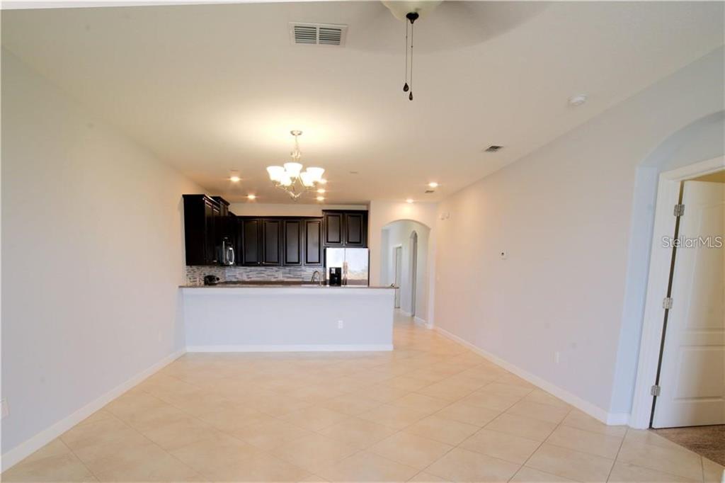An open-concept kitchen with dark cabinets and a breakfast bar overlooks a tiled living area — 1251 LONG COVE LOOP UNIT 1251, DAVENPORT, FL