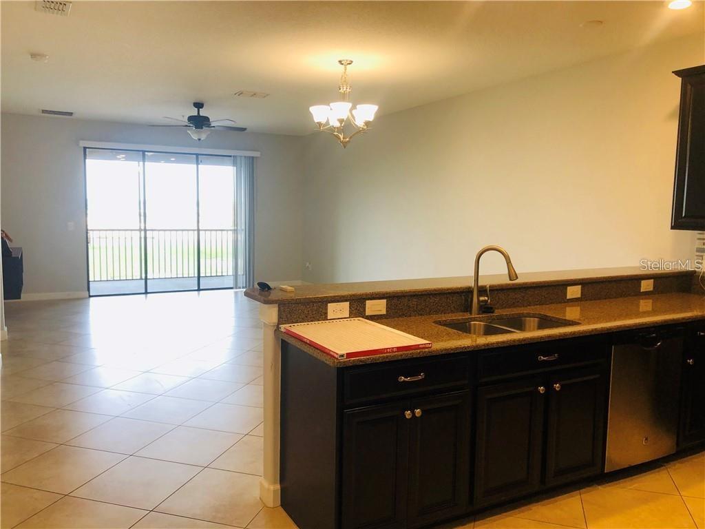 A kitchen with dark cabinets and granite countertops overlooks an open living area with tile — 1251 LONG COVE LOOP UNIT 1251, DAVENPORT, FL