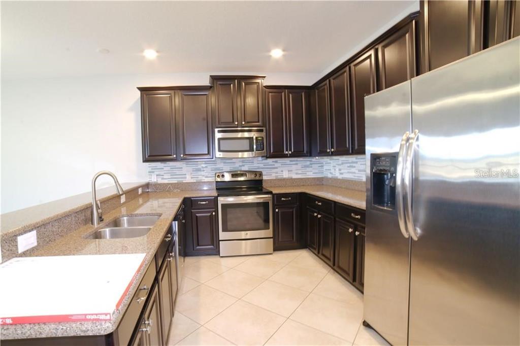 A kitchen features dark wood cabinets, granite countertops, stainless steel appliances, and tile flooring — 1251 LONG COVE LOOP UNIT 1251, DAVENPORT, FL