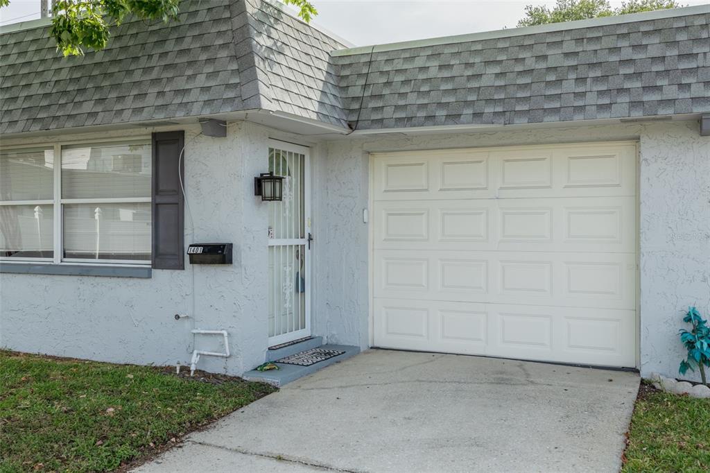 A single-story house exterior features a white garage door, a front door with a security gate — 1401 CARA DRIVE UNIT 1401, LARGO, FL