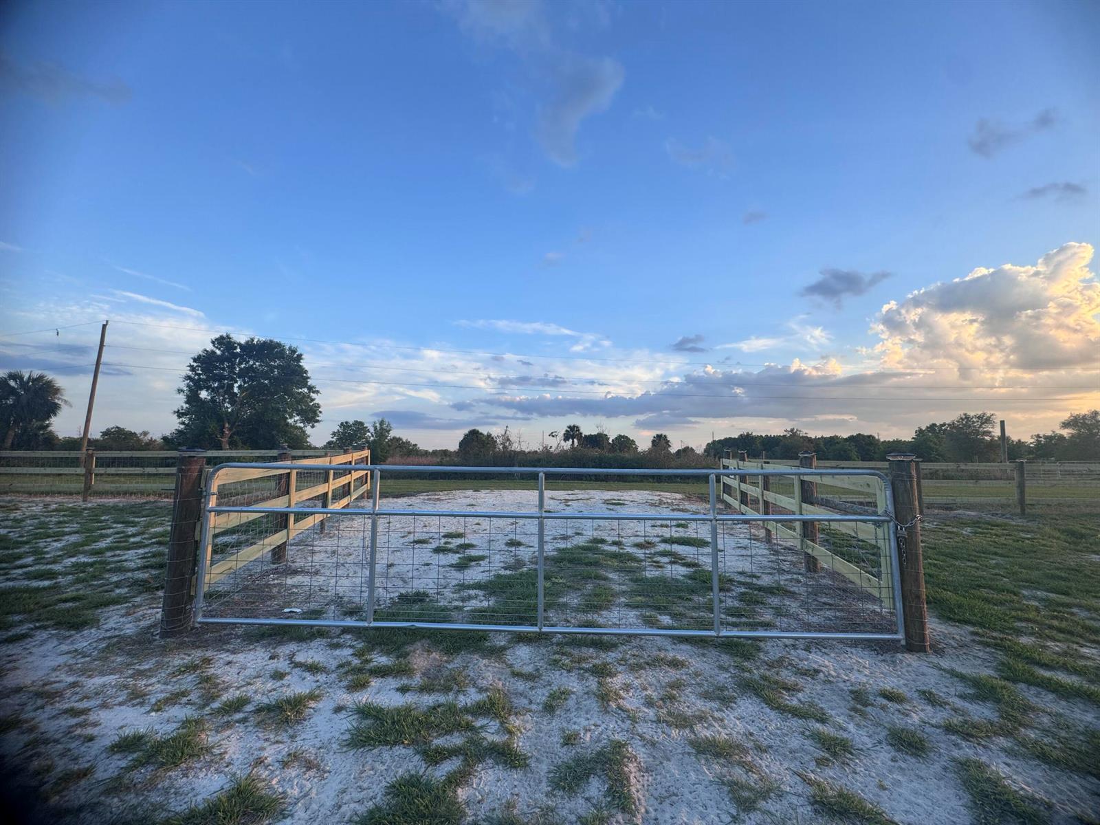 A metal gate stands between wooden fence posts in a sandy, fenced-in outdoor area — 14769 NW 244th Street, Okeechobee FL 34972, OKEECHOBEE, FL