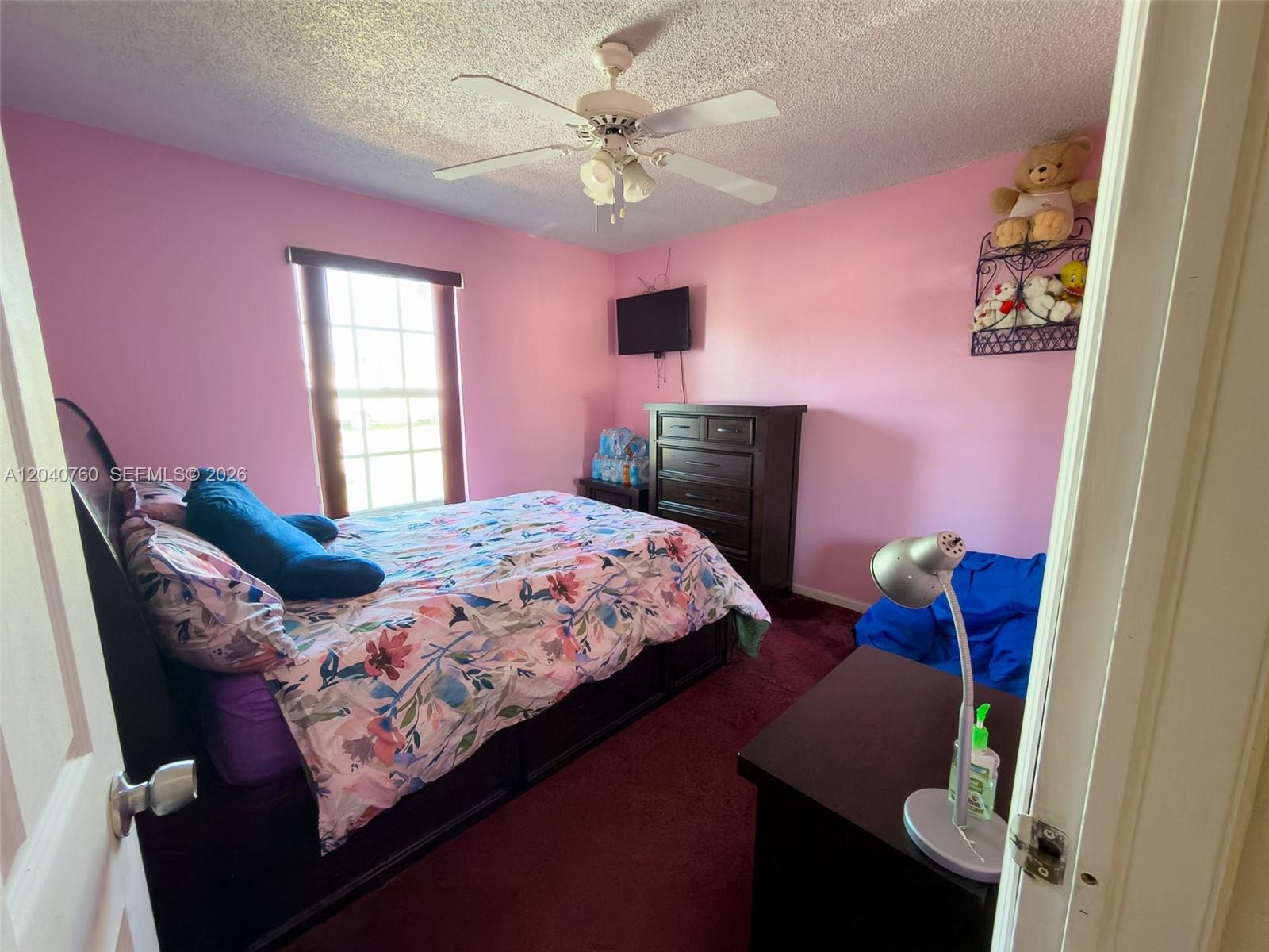 A bedroom features pink walls, a floral bedspread, dark furniture, and a ceiling fan — 19251 NW 33rd Ave, Miami Gardens FL 33056, MIAMI GARDENS, FL
