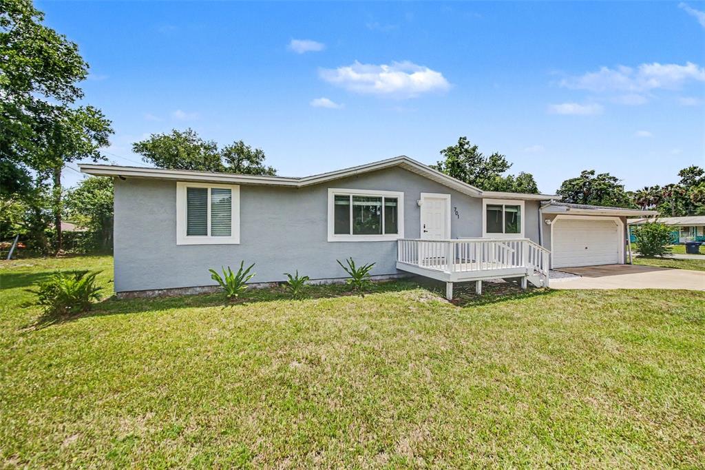 A single-story gray house with a white front deck, attached garage, and grassy yard — 701 E WOODLAND STREET, BUNNELL, FL