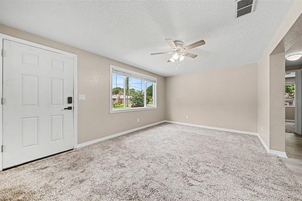 A carpeted living room features a white front door, a ceiling fan, and a window — 701 E WOODLAND STREET, BUNNELL, FL