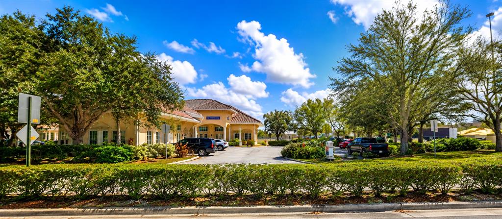 A beige commercial building with a tiled roof sits behind a manicured hedge and trees — 5275 OFFICE PARK BOULEVARD, BRADENTON, FL
